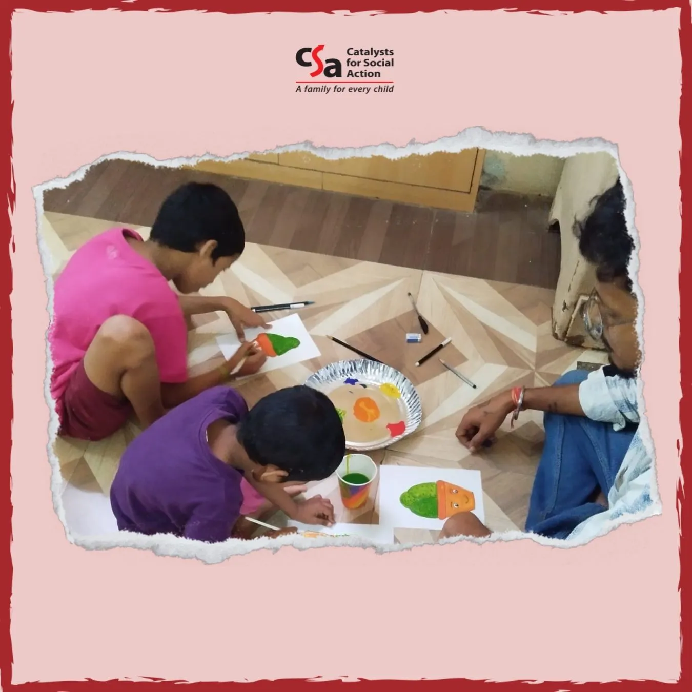Three children and an adult sit on the floor engaging in a painting activity. Each child is painting a colorful vegetable-like shape on paper using bright paints from a shared palette. Art supplies like brushes, pens, and cups of water are scattered around. The scene is framed with a torn paper effect and features the logo of "Catalysts for Social Action" with the tagline "A family for every child" at the top.